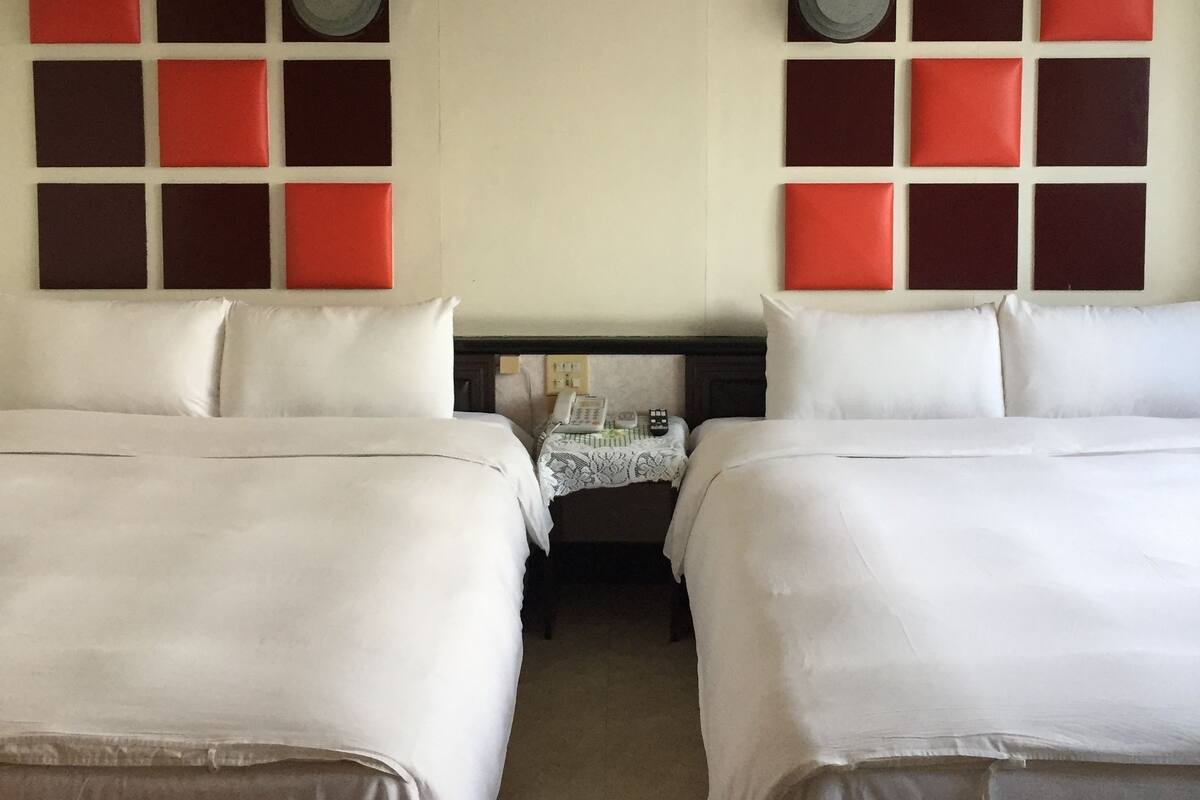 A hotel room with two beds, a small table with a telephone, and a wall with a red and black pattern.