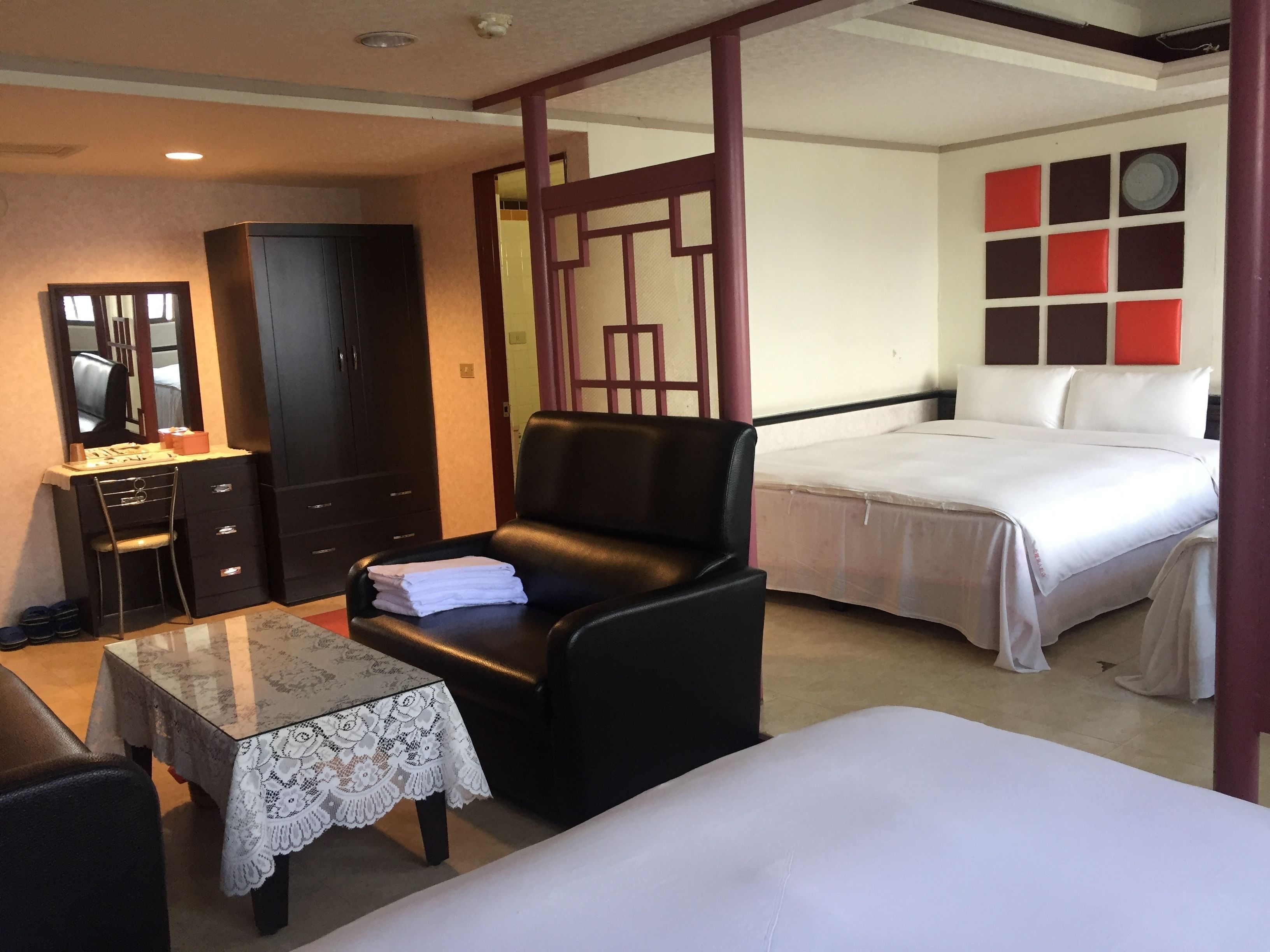 Una habitación de hotel con una cama, un escritorio con silla, un armario y una mesa con mantel de encaje.