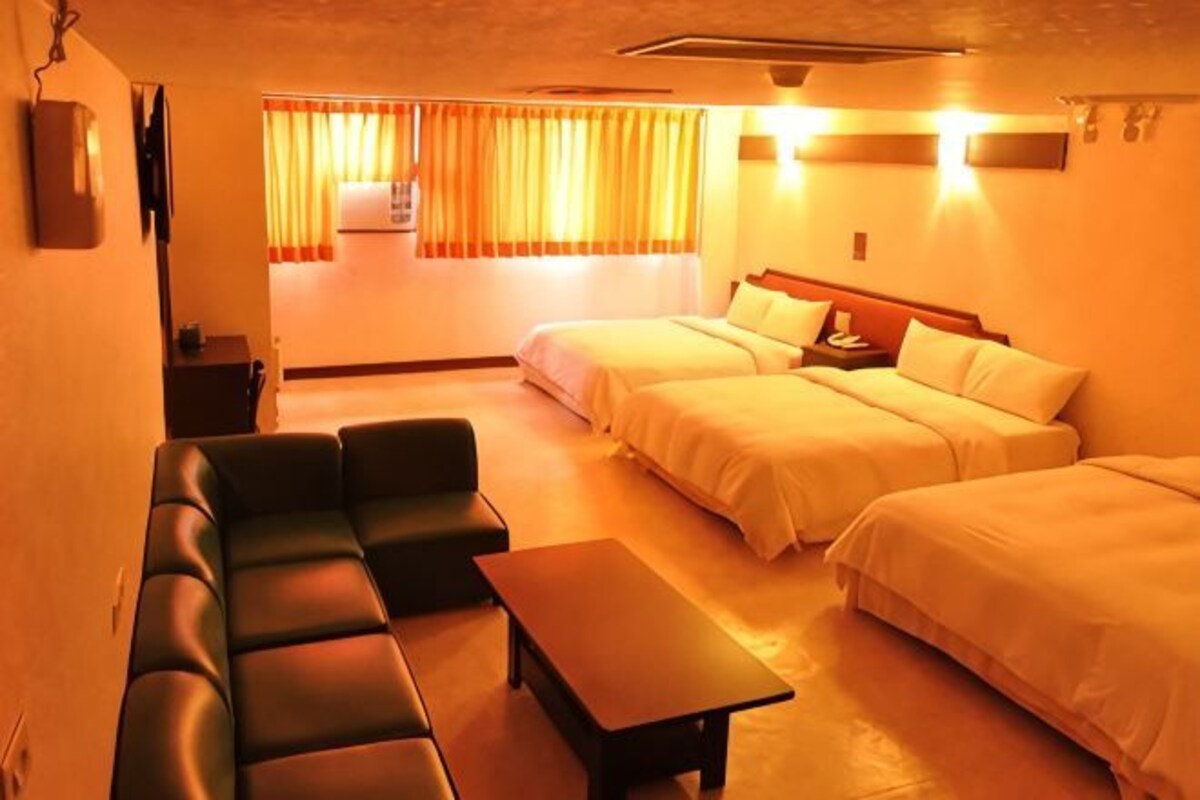 A hotel room with two beds, a sofa, a table, and a window with curtains.