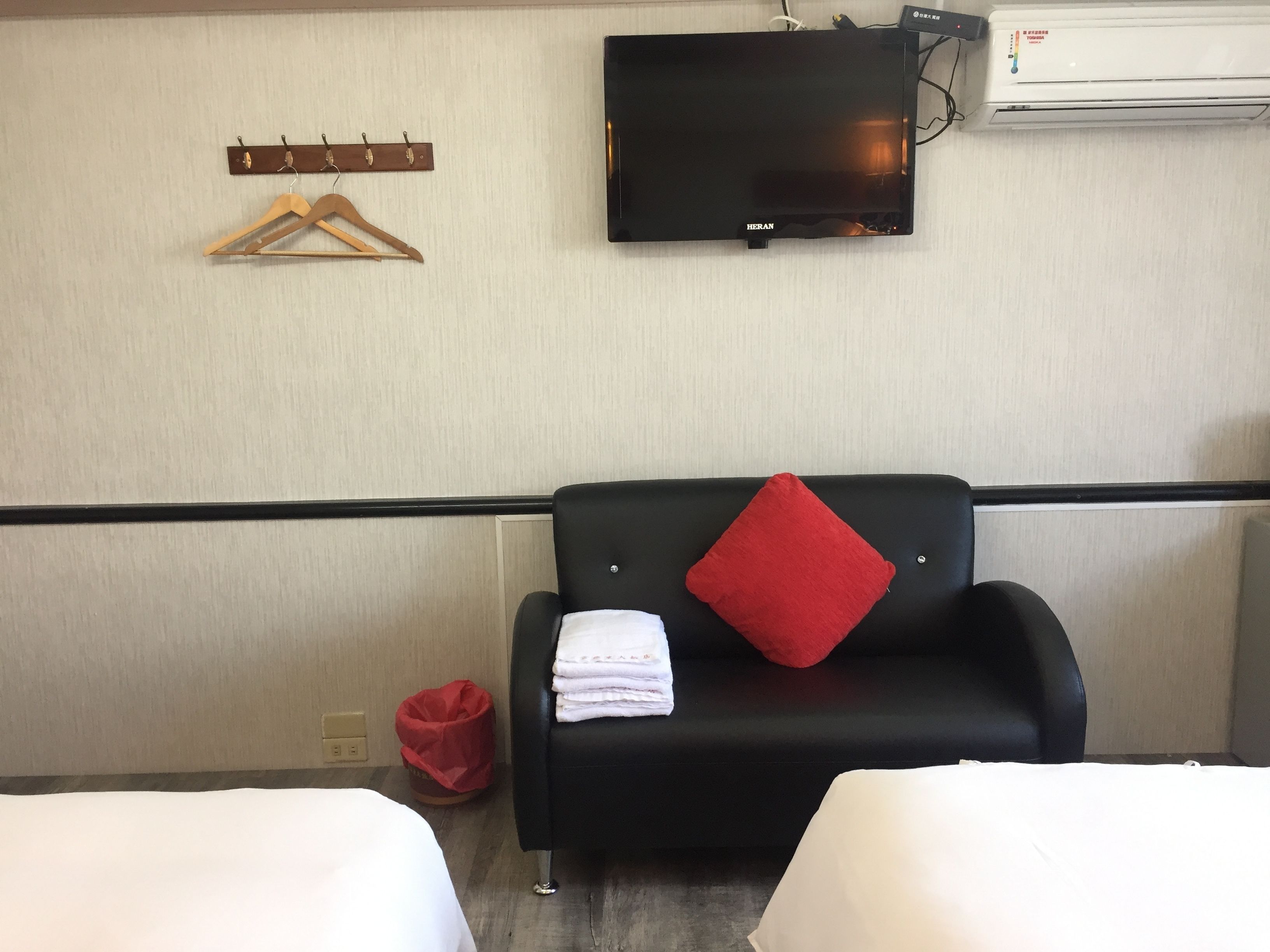 A hotel room with a black sofa, a red pillow, and a TV mounted on the wall.