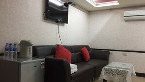 A room with a black sofa, a small table with a lace tablecloth, a refrigerator, a kettle, and a flat-screen TV mounted on the wall. - King Lo Tung Hotel (Luodong)