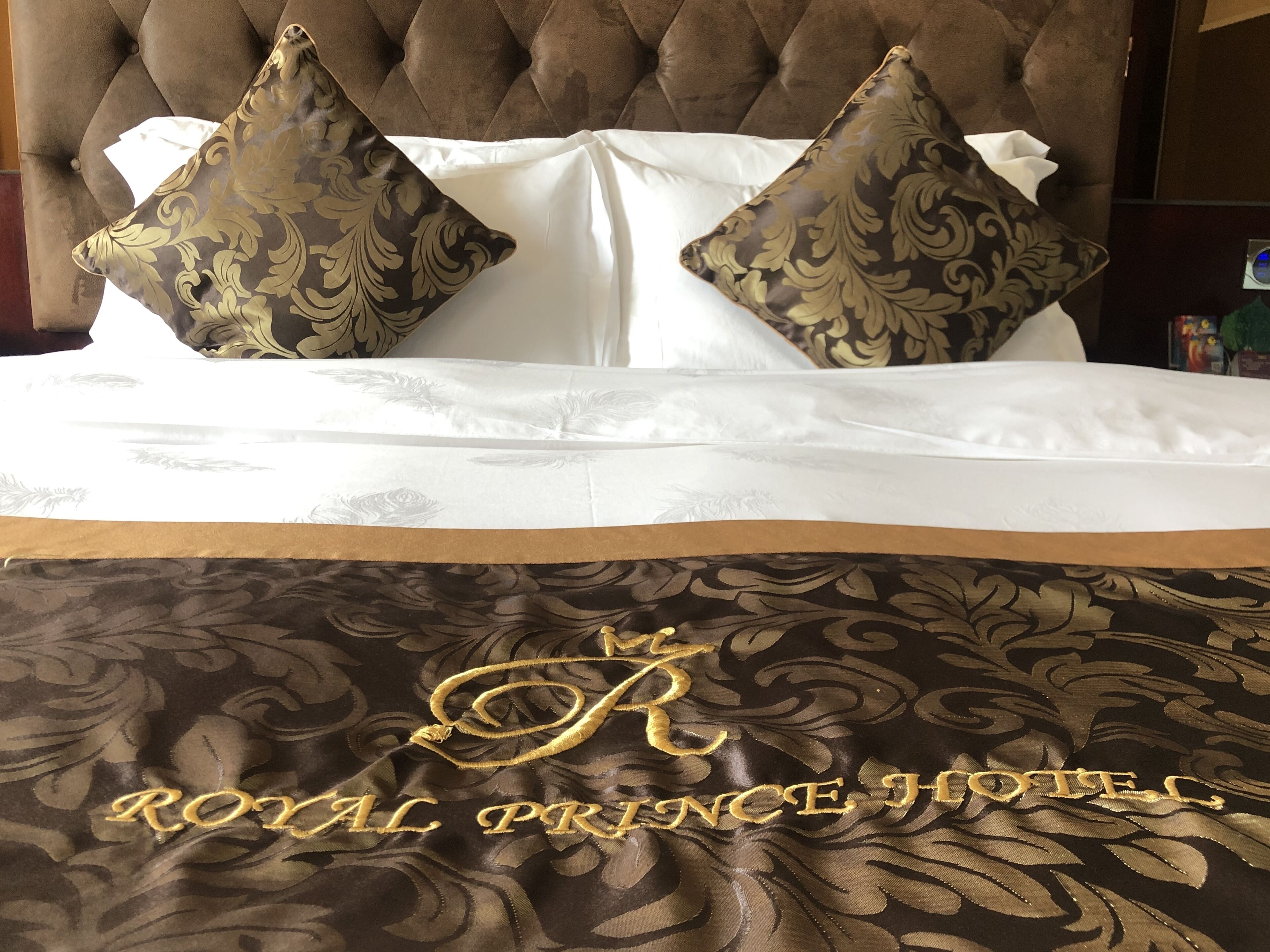 A bed with a tufted headboard, two patterned pillows, and a bedspread with embroidered text.