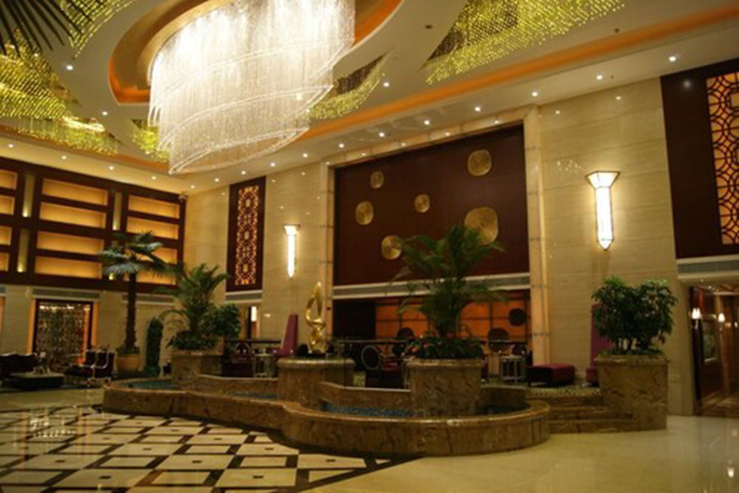 A spacious lobby with a large chandelier, decorative wall panels, and several potted plants.