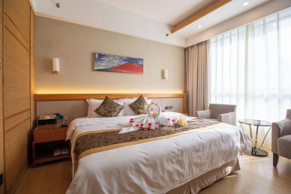A hotel room with a large bed, a desk, a chair, and a view of the city.