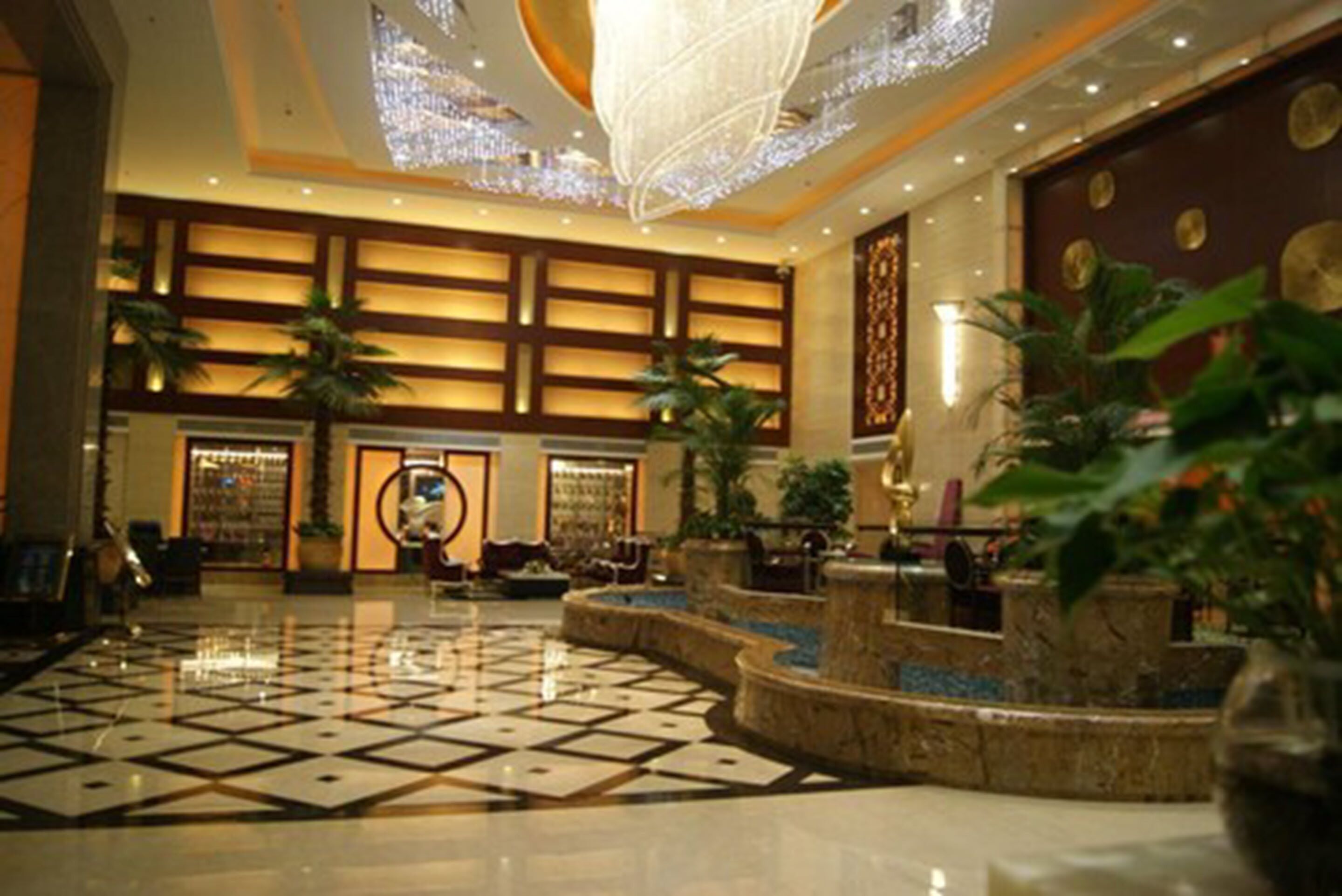 A spacious lobby with a polished floor, a large chandelier, and several potted plants.