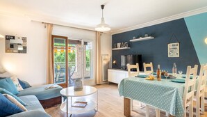 A living room with a sofa, a round coffee table, and a dining area with a table set for two. There is a TV on a stand and a balcony with a view of greenery. - Cosy apartment for 4 people with A/C, WIFI, TV and terrace (Sanary-sur-mer)