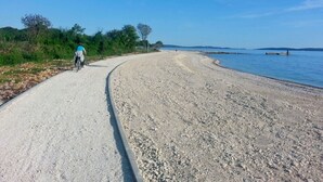 A gravel path beside a calm body of water with a cyclist in the distance. - Lovely apartment for 6 guests with A/C, WIFI, TV, terrace and pets allowed (Peroj)