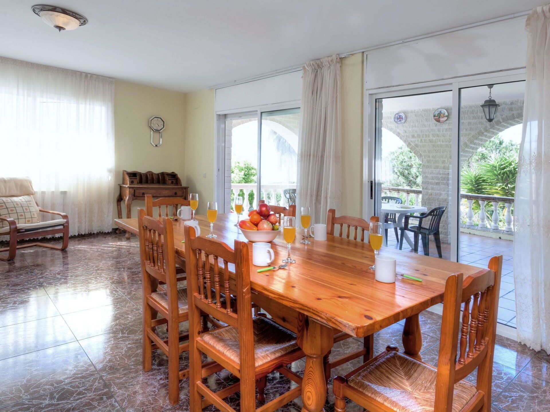 Un comedor con una mesa y sillas de madera, un frutero y vasos de jugo de naranja.