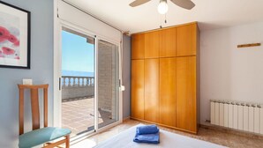 Une chambre à coucher comprenant un lit, une chaise, une armoire et une vue sur la mer, visible à travers une porte vitrée.