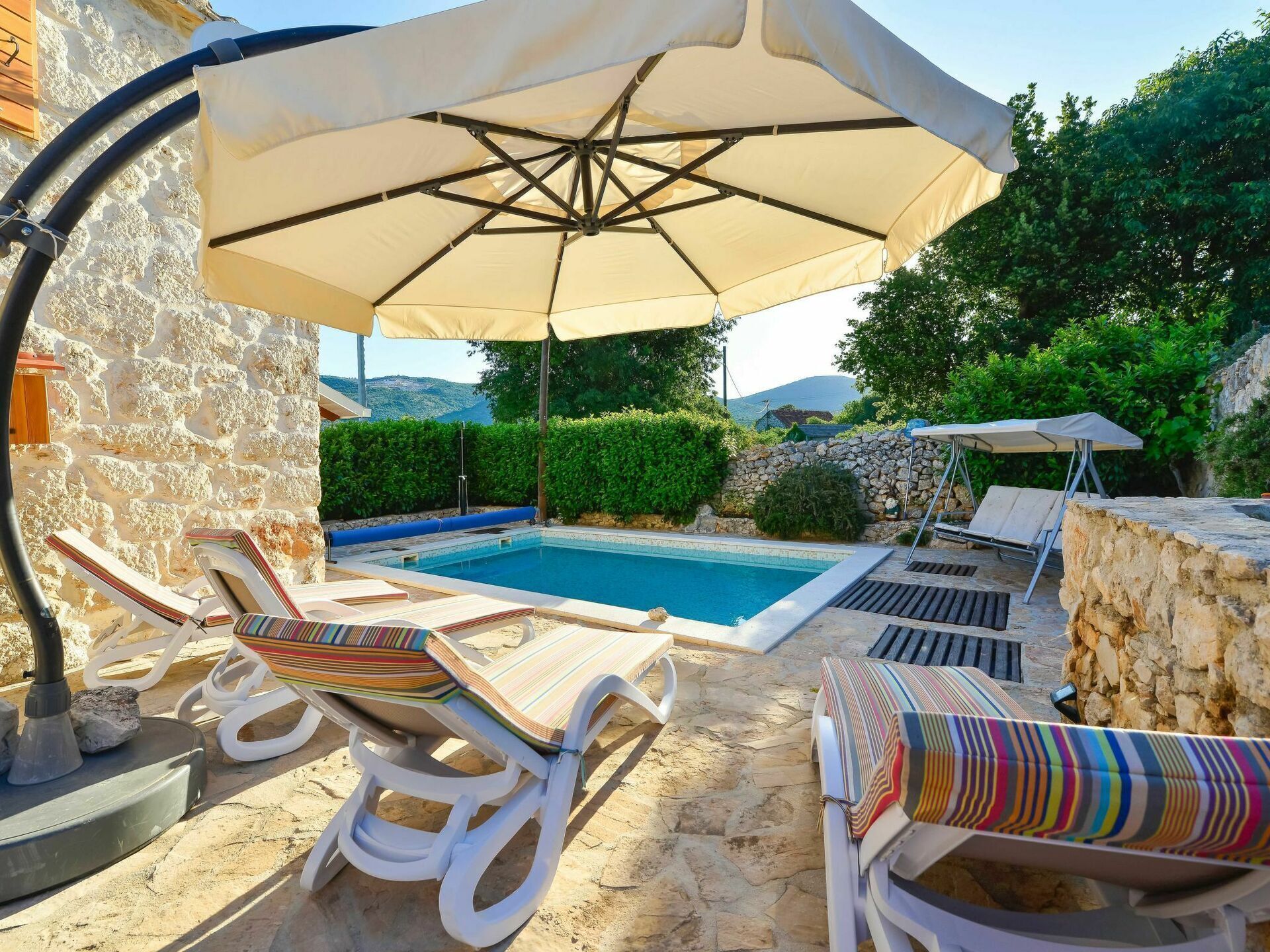 Un espace aménagé au bord de la piscine, avec des chaises longues, un grand parasol et un mur en pierre.