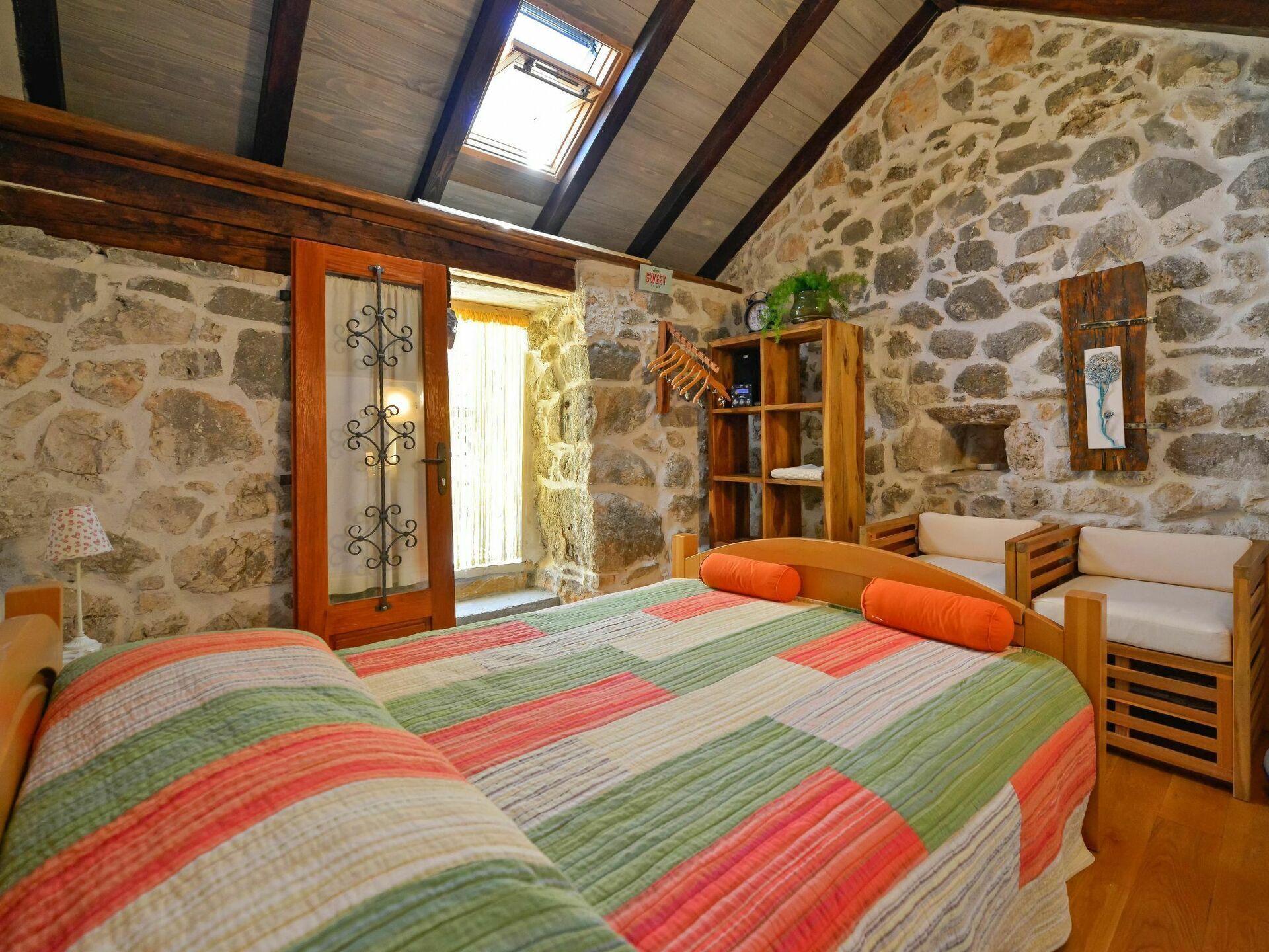 A bedroom with a stone wall, wooden furniture, a bed with a colorful quilt, and a skylight.