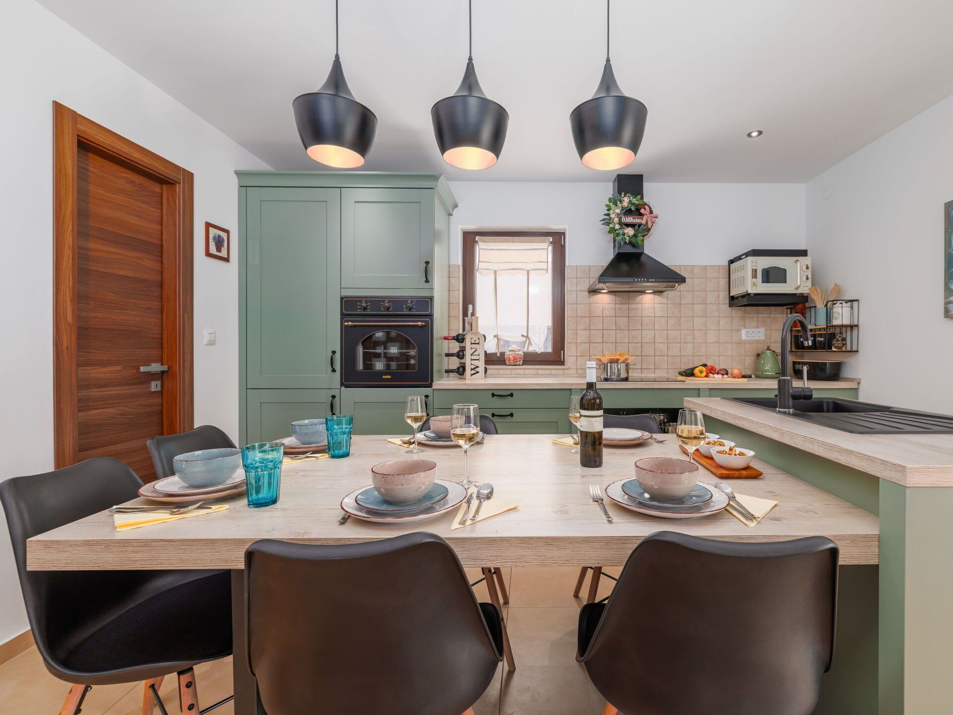 Una cucina moderna con isola centrale, illuminazione a sospensione e vista sull'area pranzo.