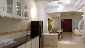 A modern kitchen with white cabinets, a black refrigerator, and a dining area with a table and chairs. - BB Villas - 5 min Jonker Melaka (Malacca City)