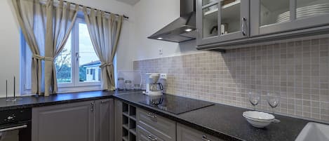 A modern kitchen with grey cabinets, a black countertop, a coffee maker, and a window with curtains.