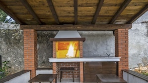 Una chimenea de ladrillo exterior con chimenea, rodeada de bancos de madera y un suelo de baldosas.