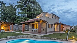 Una casa moderna de dos pisos con piscina, mobiliario exterior y zona de barbacoa.