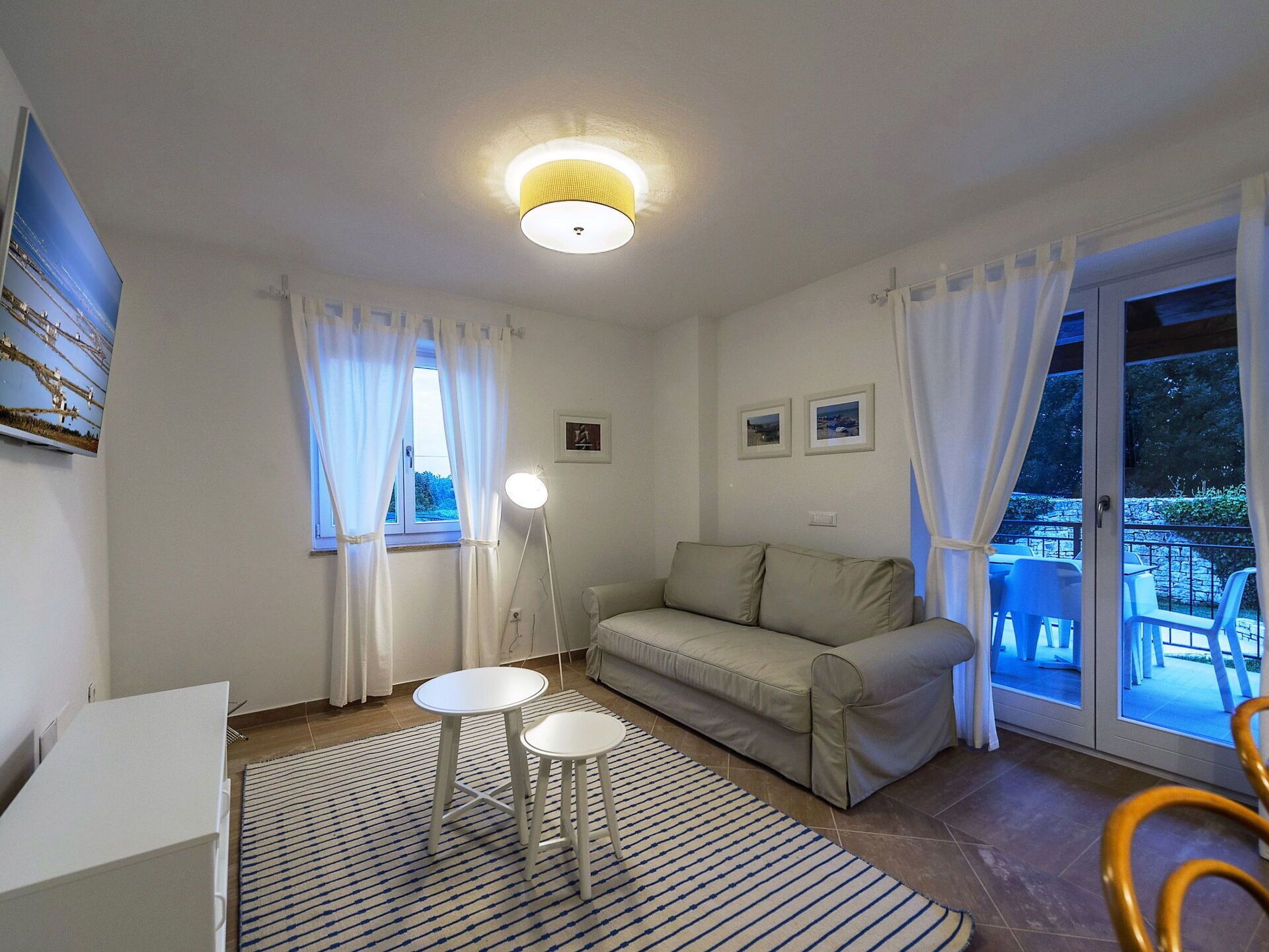 A living room with a sofa, two small tables, a lamp, and a view of the outside.