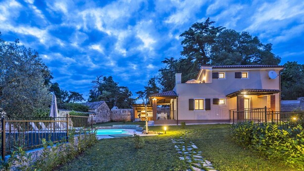 Una casa de dos pisos con piscina, camino de piedra y zona exterior bien iluminada.