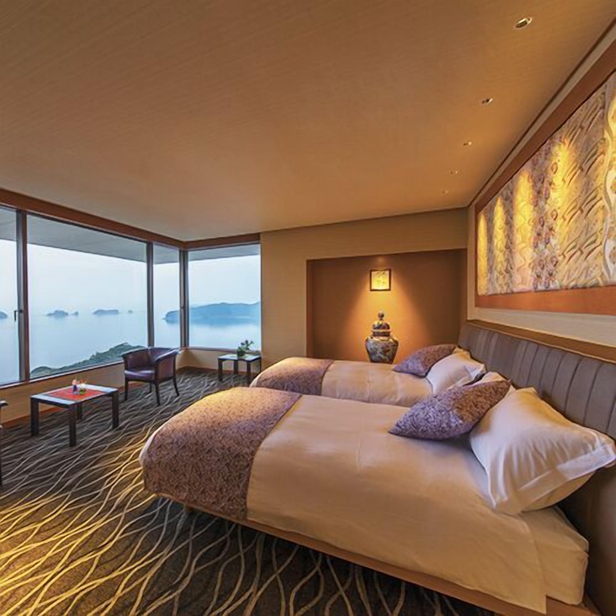 A hotel room with a large bed, a small table, a chair, and a view of the sea.