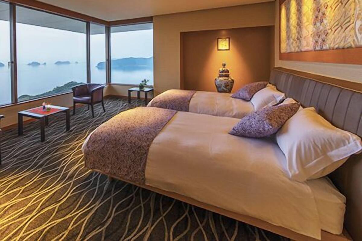 A hotel room with a large bed, a small table, a chair, and a view of the sea.