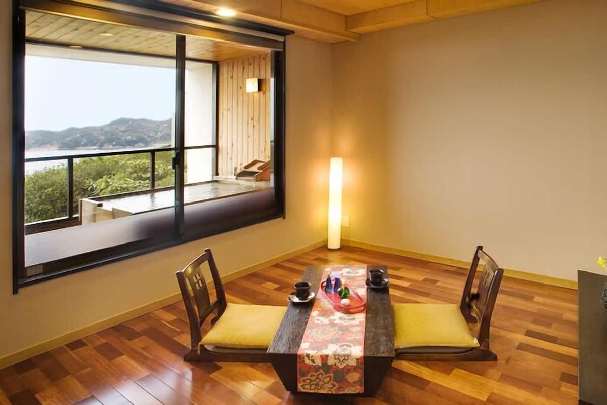 A room with a large window, a table with chairs, and a floor lamp.