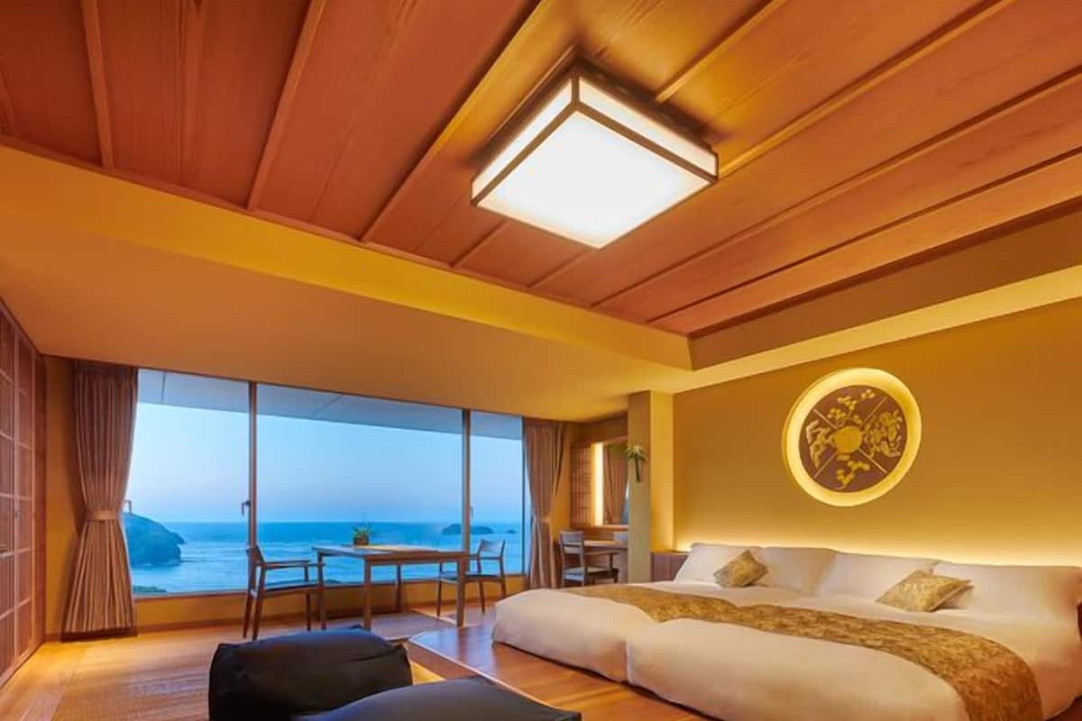 A bedroom with a large bed, a dining table, and a view of the sea.