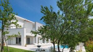 Una casa moderna de dos pisos con piscina, un porche cubierto y un césped bien cuidado.