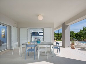 Un espacio moderno para comer al aire libre con mesa y sillas, vista a la cocina y zona junto a la piscina.