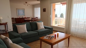 Ein Wohnzimmer mit einem grünen Sofa, einem Holztisch und einem Essbereich im Hintergrund.