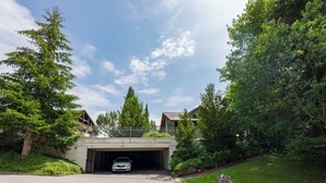 A residential driveway leading to a garage under a covered area, surrounded by lush greenery and trees. - Beautiful apartment for 4 guests with WIFI, TV, balcony and panoramic view (Mauren)