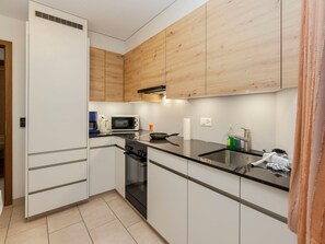 Une cuisine de taille réduite avec des meubles blancs, un plan de travail noir, un four à micro-ondes, une cuisinière et un évier.