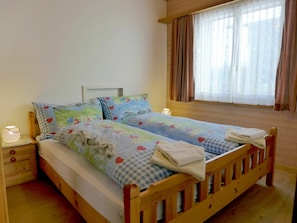 A double bed with floral bedding, a bedside table with a lamp, and a window with curtains.