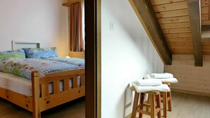 A wooden bed with a floral bedspread, a wooden headboard, and a nightstand with a lamp. There is a wooden stool with a towel on it. - Beautiful apartment for 4 guests with WIFI, TV, balcony and panoramic view (Mauren)
