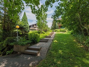 Un chemin menant à un bâtiment à l’architecture moderne, entouré d’une végétation luxuriante et sous un ciel dégagé.