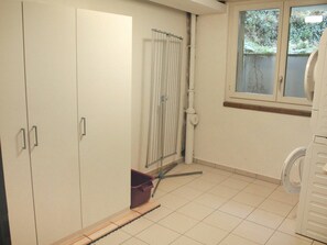 Une pièce avec une armoire blanche, une fenêtre donnant sur un espace verdoyant et un lave-linge.