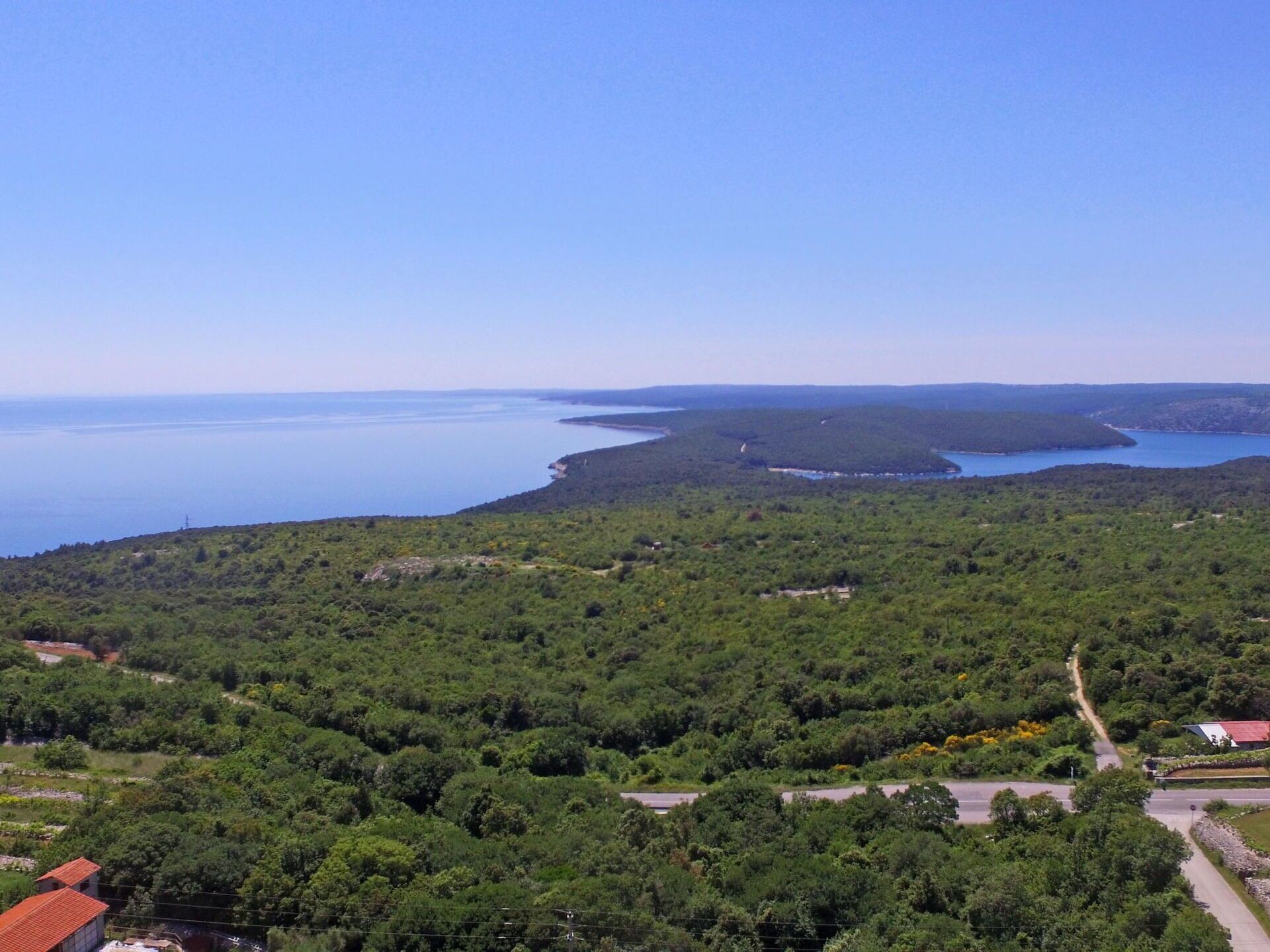 A coastal landscape with dense greenery, a clear sky, and a body of water.