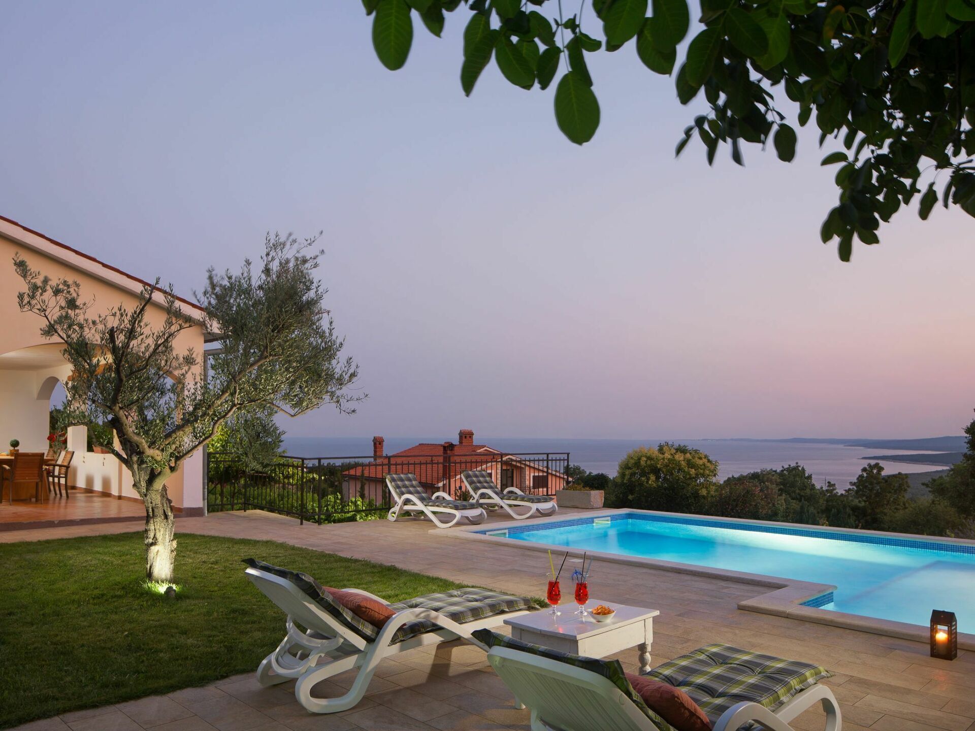 A poolside area with lounge chairs, a table with drinks, and a view of the sea.