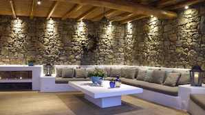 Interior de una pared de piedra con techo de madera, un sofá blanco, una mesita de café blanca y una pequeña planta.