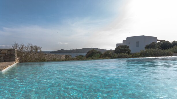 Piscina cristalina con vista a un edificio blanco y colinas lejanas.