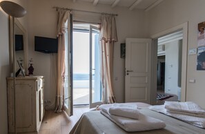 A bedroom with a bed, a dresser, a television, and a view of the beach through an open door.