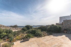A rooftop garden with stone walls, potted plants, and a view of the sea.