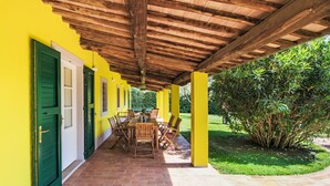 A covered patio with a brick floor, wooden tables and chairs, and a yellow wall with green shutters. - Beautiful private villa for 10 guests with private pool, WIFI, A/C, TV, patio and pets allowed (San Vincenzo)