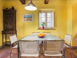 A dining area with a table, chairs, a potted plant, a window, and a wall-mounted picture.