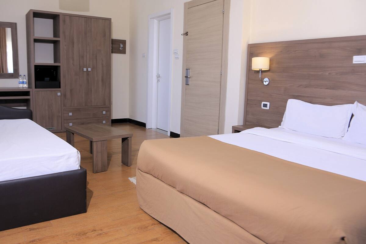 A hotel room with two beds, a wooden wardrobe, a small table, and a mirror.