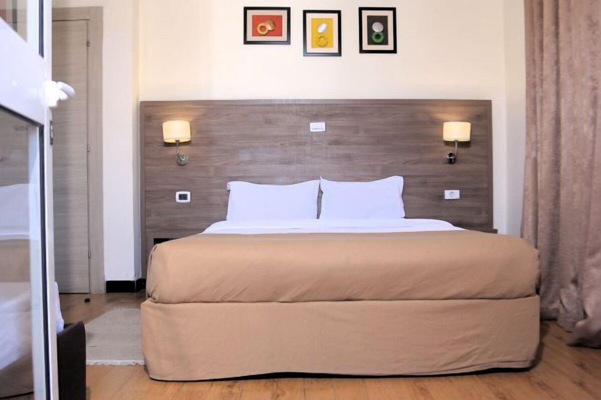 A hotel room with a large bed, two wall-mounted lamps, and three framed pictures on the wall.