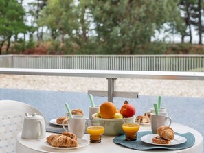Ein Frühstückstisch auf einer Terrasse mit Blick auf Bäume und einer Brüstung.