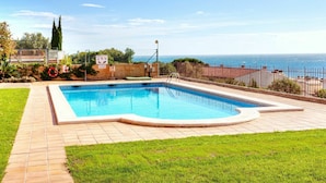 A rectangular swimming pool with a tiled deck, surrounded by a low fence, and a clear view of the sea in the background.