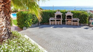 A patio with two outdoor grills, a pool, and a view of the sea.