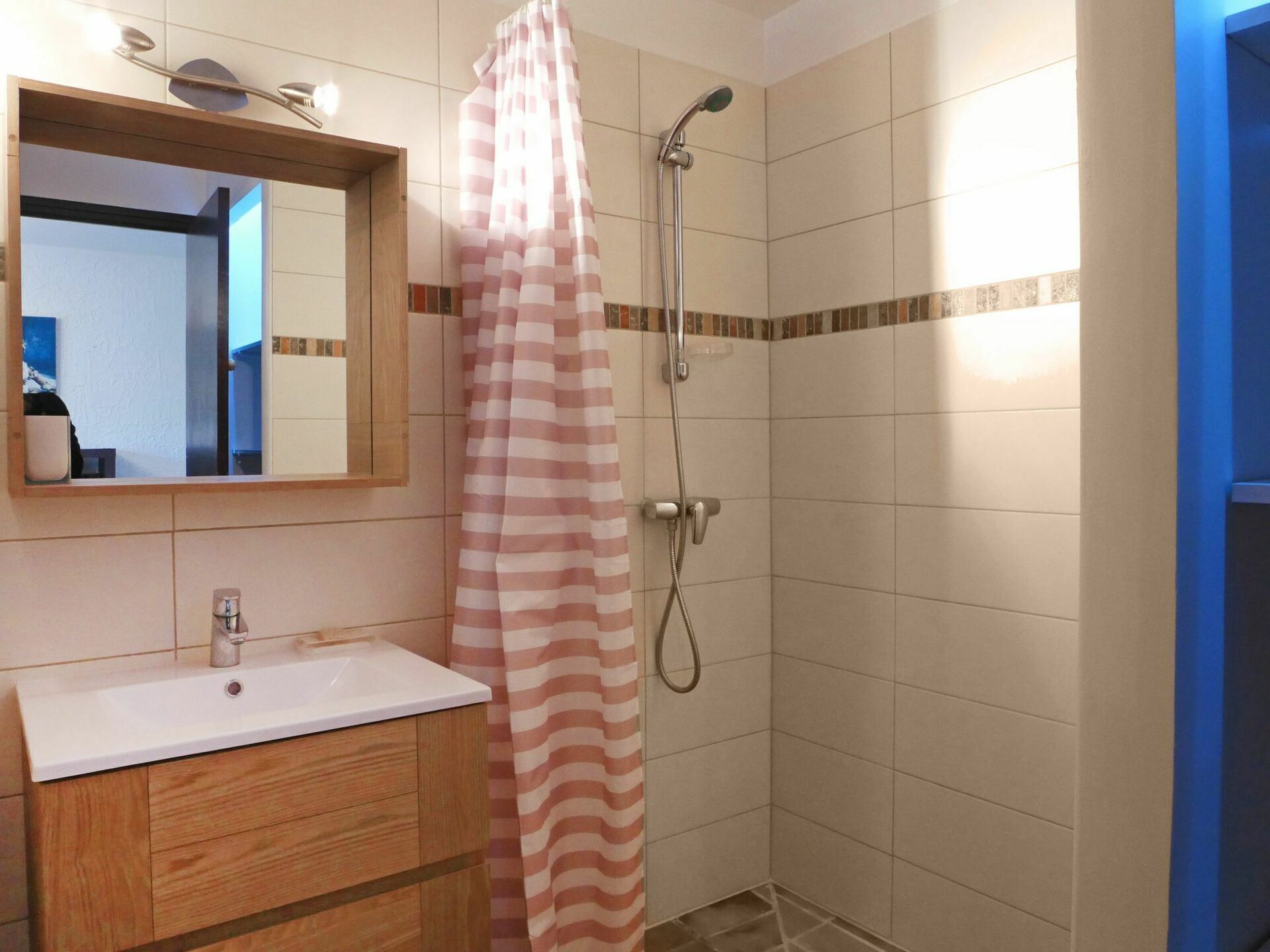 A bathroom with a wooden vanity, a mirror, a shower with a striped curtain, and tiled walls.