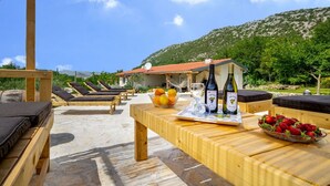 Une terrasse en bois avec des chaises longues et une table où sont disposées des bouteilles de vin et des fruits.